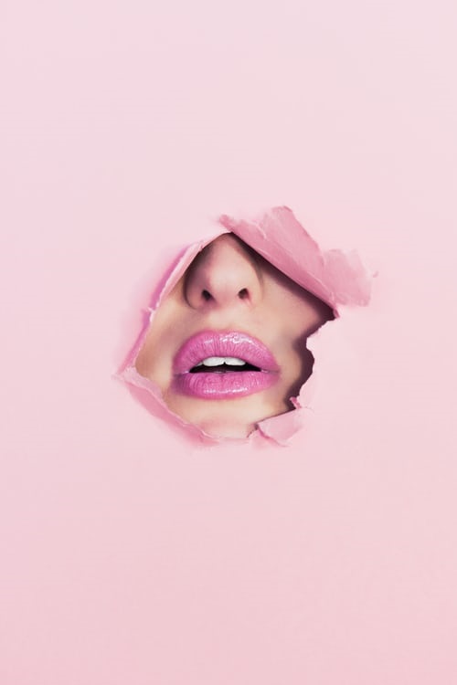 Face with makeup breaking through a wall