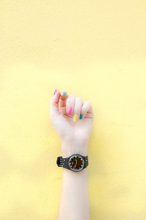 Arm with wristwatch and colorfully painted nails
