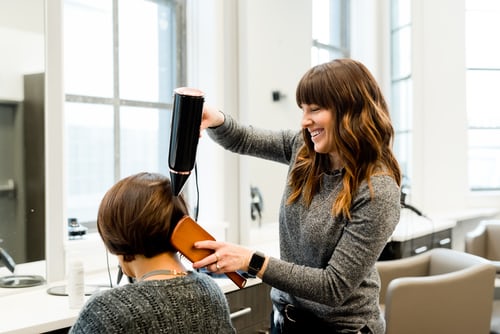 Hairdresser blow drying and combing client's hair