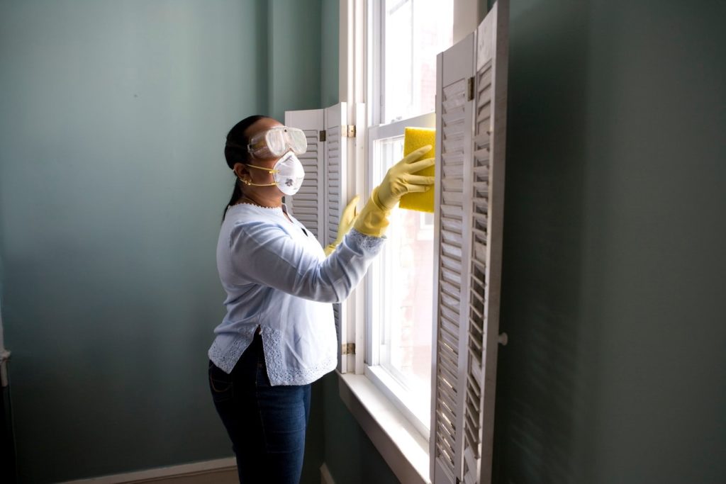 Home cleaner with mask and goggles on cleaning a window