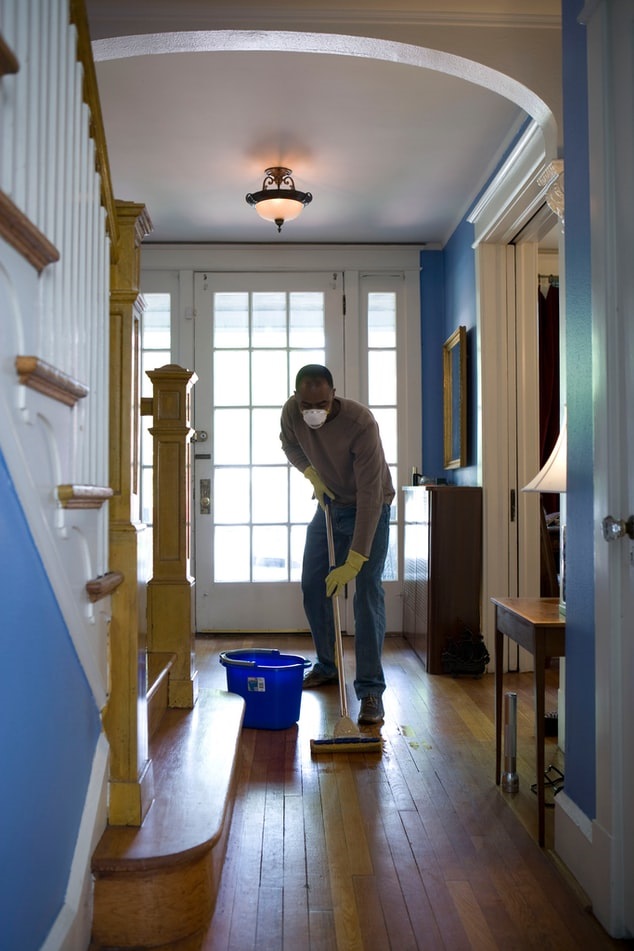 Home cleaner wearing mask while cleaning wood floor