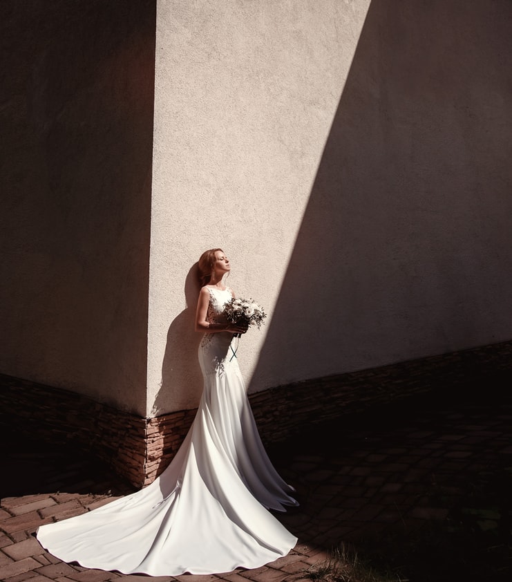 Bride standing up against a wall in the sunlight holding her bouquet