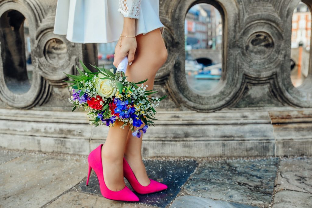 Bride holding a bouquet by her legs while walking on a bridge