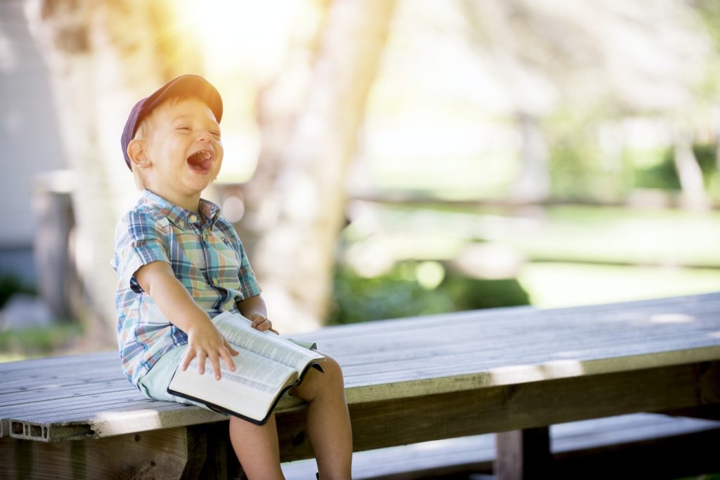 Young boy laughing while sitting on a bench with a book in his lap