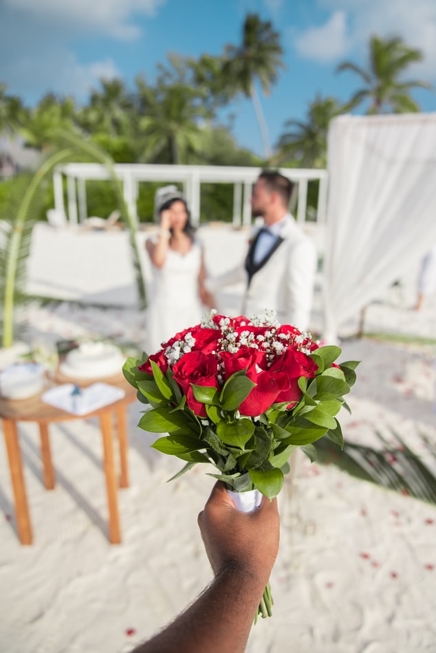 Person holding a bouquet with the bride and groom standing in the background