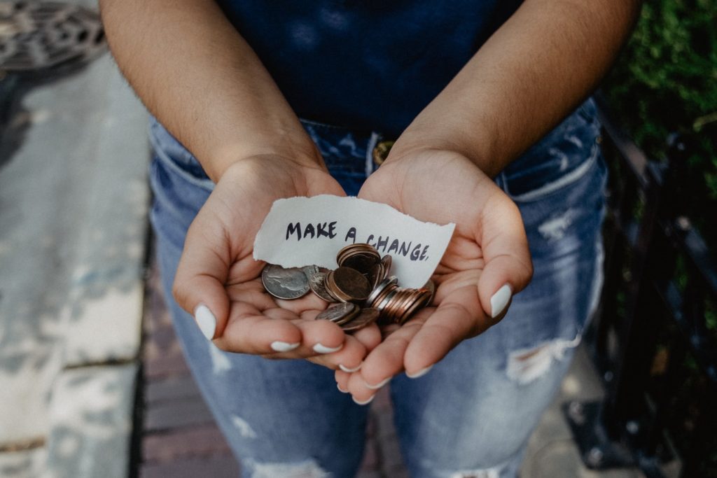 A person holding coins with a piece of paper that reads "Make a change"