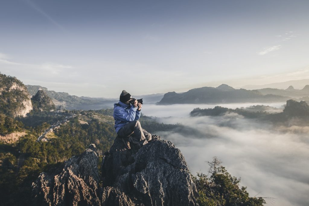 Landscape photographer sitting on a jagged mountaintop to capture high altitude images