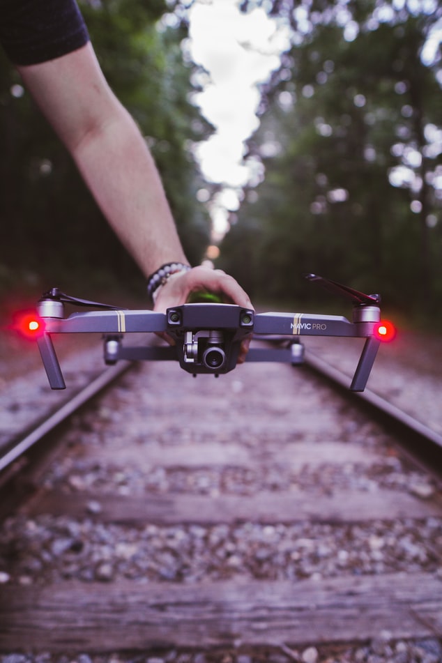 Aerial/drone photographer holding a drone over train tracks