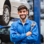 Portrait of smiling male mechanic technician holding wrench in arms crossed at auto garage. repair and maintenance career. after service, checking car damage broken part