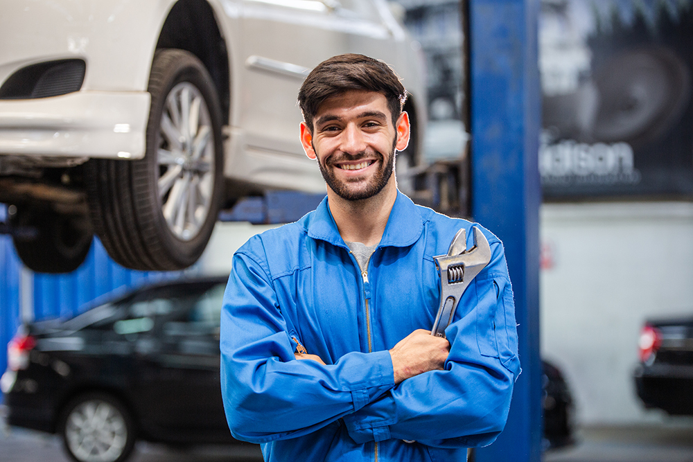 Portrait of smiling male mechanic technician holding wrench in arms crossed at auto garage. repair and maintenance career. after service, checking car damage broken part