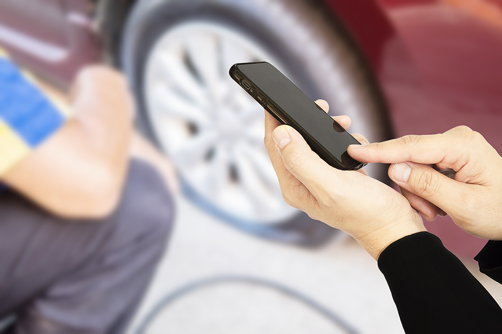 Man is using mobile phone calling somebody over car flat tire background